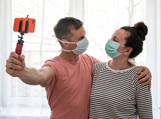Couple in disposable masks taking selfie at home. Social distancing - Zdjęcie, obraz