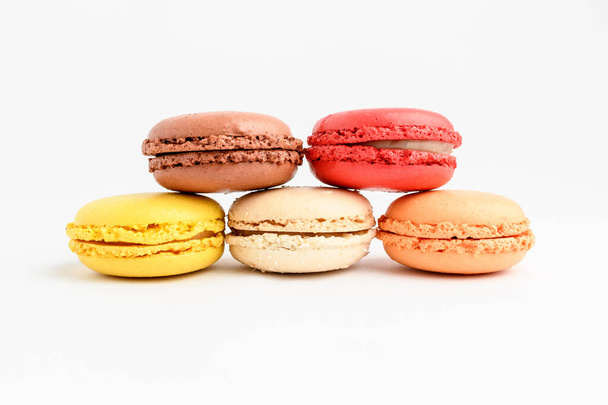 Five sweet French macarons with different aromas, isolated on white, flavours of strawberries, lemon, caramel, vanilla, orange and chocolate, tasty dessert in pastel colors on a table - Fotografie, Obrázek