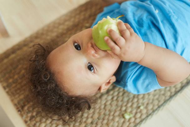 Πάνω από άποψη πορτρέτο του χαριτωμένα μικτή φυλή νήπιο τρώει πράσινο μήλο, ενώ κοιτάζοντας κάμερα, αντίγραφο χώρο - Φωτογραφία, εικόνα