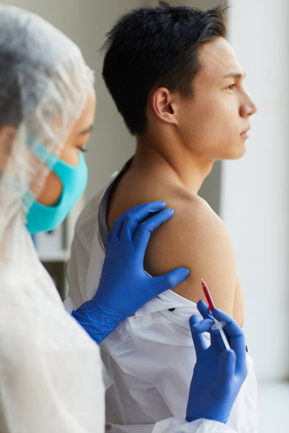 Προσωπογραφία νοσοκόμου που κάνει εμβόλιο σε άρρενα ασθενή κατά τη διάρκεια της θεραπείας στην κλινική - Φωτογραφία, εικόνα