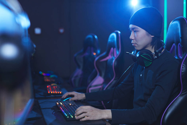 Visão lateral retrato de jovem homem asiático jogando videogames em cibernético escuro como interior, espaço de cópia
 - Foto, Imagem