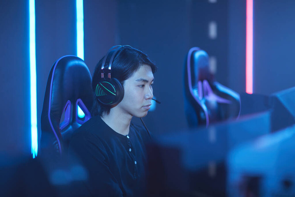 Seitenansicht Porträt eines jungen asiatischen Mannes, der mit Headset spricht, während er Videospiele im dunklen Raum spielt, Kopierraum - Foto, Bild