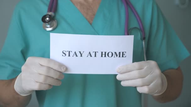 Ręka lekarza trzyma zdjęcie z napisem w domu podczas epidemii koronawirusa. Lekarz pokazuje plakat z apelem o samoizolację. Koncepcja bezpieczeństwa życia z pandemii COVID-19 - Materiał filmowy, wideo
