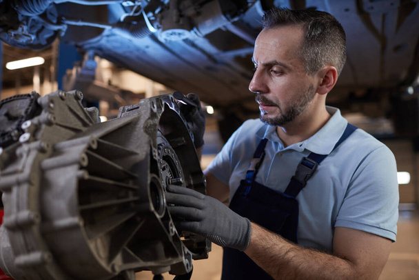 Waist up portrait of muscular car mechanic inspecting car part in auto repair shop, copy space - Photo, Image