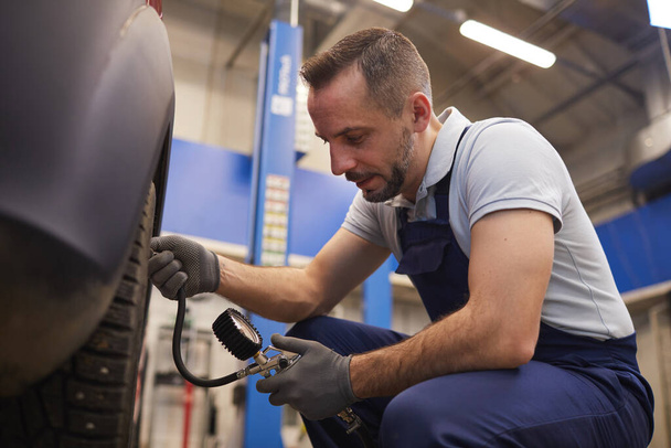 Portrait latéral du mécanicien automobile vérifiant la pression dans les pneus lors de l'inspection du véhicule dans l'atelier de garage, espace de copie
 - Photo, image