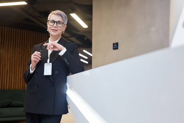 Portrait of mature business manager wearing badge while standing on staircase and looking at camera in minimal interior, copy space - Fotoğraf, Görsel
