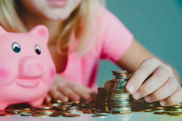 child counting coins and saving money, kid puts coins into piggy bank - Fotó, kép