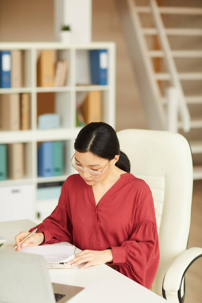 Vertikales Porträt einer erfolgreichen asiatischen Geschäftsfrau, die am Schreibtisch in einem modernen weißen Büro arbeitet, Kopierraum - Foto, Bild
