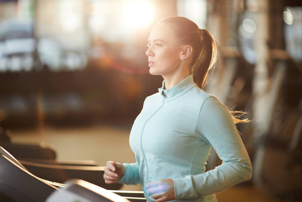 Портрет спортивної молодої жінки, що біжить на біговій доріжці під час кардіо-тренувань у сонячному спортзалі, блимає лінза
 - Фото, зображення