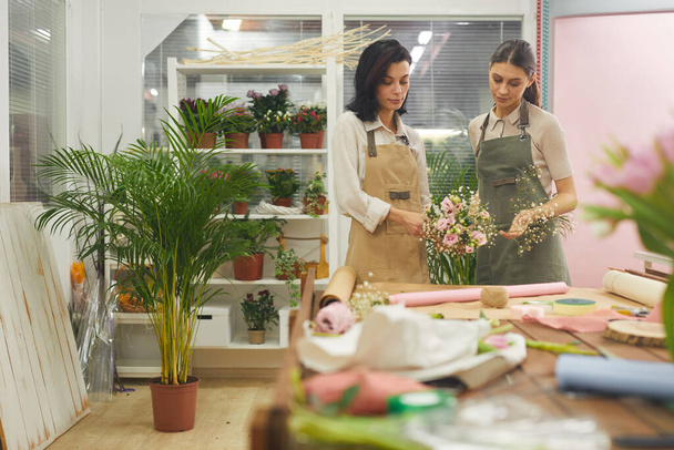 Waist up portrait of two florists arranging bouquets and floral composition while working in flower shop, copy space - 写真・画像