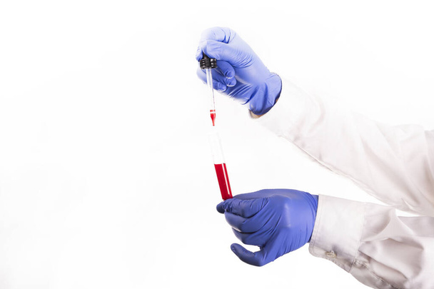 Medical worker's hands with protective, blue, nitrile gloves, holding a test tube and taking a blood sample with a pipette, on a white background, with copyspace. Coronavirus test. A corona pandemic.  - Fotó, kép