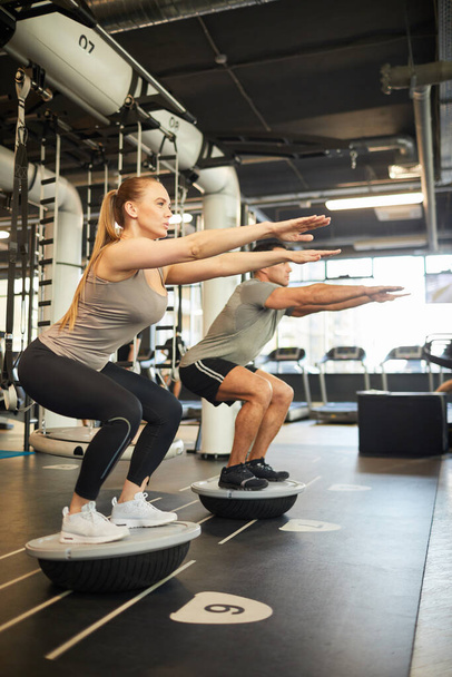 Pełna długość widoku bocznego w sportowej pary robi ćwiczenia równowagi podczas treningu w nowoczesnej siłowni, przestrzeń kopiowania - Zdjęcie, obraz