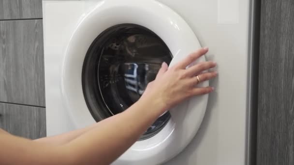 結婚指輪を持つ女性の手は洗濯機にジーンズを入れて.洗濯機を搭載。洗濯機に衣類をロードします。衣類洗濯機をロードします。洗濯の準備 - 映像、動画