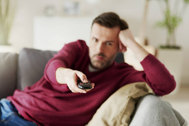 Unatkozó ember kezében egy távirányítóval és TV-t néz - Fotó, kép