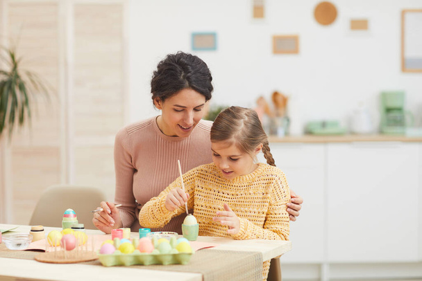 Portrait de mère aimante et fille peinture oeufs de Pâques couleurs pastel assis à la table dans l'intérieur de la cuisine confortable, espace de copie
 - Photo, image