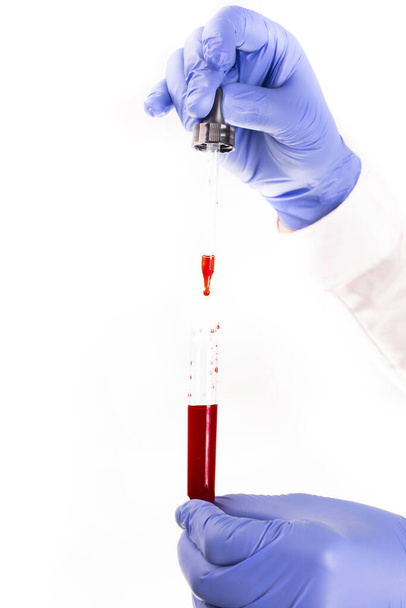Medical worker's hands with protective, blue, nitrile gloves, holding a test tube and taking a blood sample with a pipette, on a white background. Coronavirus test. A corona pandemic , COVID19. - Photo, Image