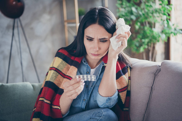 Photo of pretty displeased lady stay home alone quarantine covered checkered blanket hold pills paper napkin coronavirus infection sitting comfortable sofa living room indoors - Photo, image
