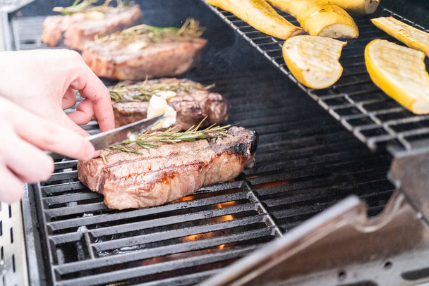 Grilling New York steak with a slice of butter and rosemary on an outdoor gas grill. - Foto, Imagem