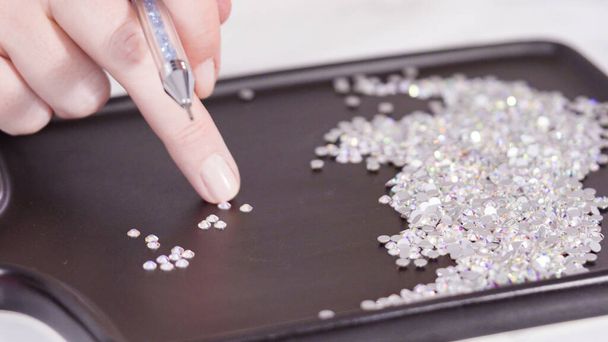 Una abundancia de diamantes de imitación blancos con la espalda plana en un tablero negro listo para un proyecto de artesanía. - Foto, imagen