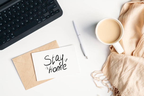 Stay home during coronavirus COVID-19 quarantine, self isolation, lockdown concept. Top view feminine workspace with laptop, coffee cup, blanket, letter, paper card with message "Stay home" - Фото, изображение