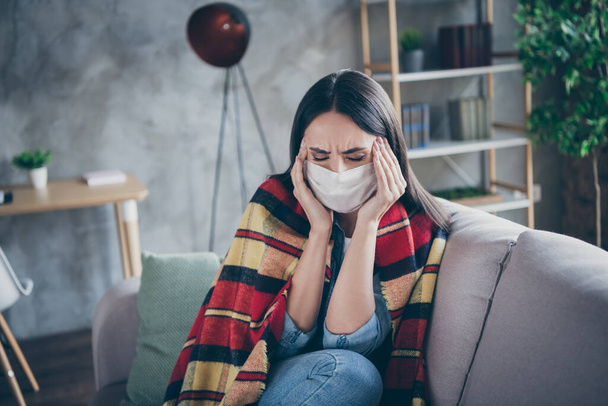 Photo of frustrated girl suffer from terrible migraine touch hands forehead have corona virus symptom plaid blanket cover body stay home wear respiratory mask sit couch in house indoors - Zdjęcie, obraz