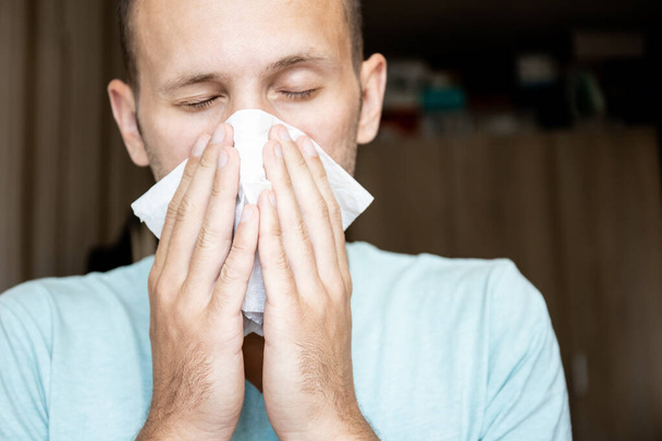 zieke jongeman blaast zijn neus in een zakdoek - Foto, afbeelding