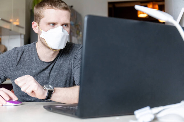giovane in maschera protettiva medica lavora in un computer portatile a casa, quarantena domiciliare durante una pandemia
 - Foto, immagini
