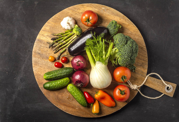 Ekspozycja świeżych warzyw organicznych na drewnianym talerzu. pomidor, pieprz, brokuły, cebula, czosnek, ogórek, bakłażan, czarny groszek, torba ekologiczna. - Zdjęcie, obraz