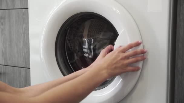 Női kéz veszi COLORED ruhák mosógép. Mosógép betöltése. Ruhákat a mosógépbe. Ruha mosógép betöltése. Mosás előkészítése - Felvétel, videó