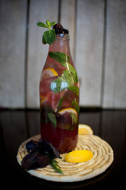 Σπιτική λεμονάδα με μούρα & πάγο λεμόνι σε διάφανο μπουκάλι νερό σταγόνες σε ξύλινο περίπτερο σε σκούρο φόντο - Φωτογραφία, εικόνα