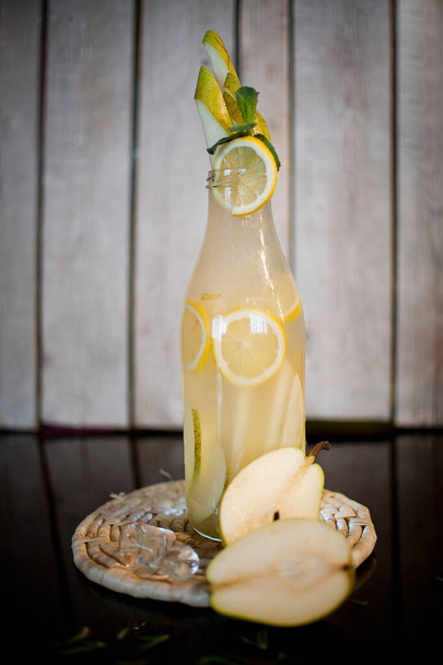 Homemade lemonade with pear lemon ice in a transparent bottle water drops on a wooden stand on a dark background - Photo, Image