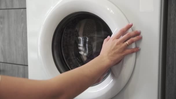 結婚指輪付きの女性の手は洗濯機から紫色の服を取ります。洗濯機を搭載。洗濯機に衣類をロードします。衣類洗濯機をロードします。洗濯の準備 - 映像、動画