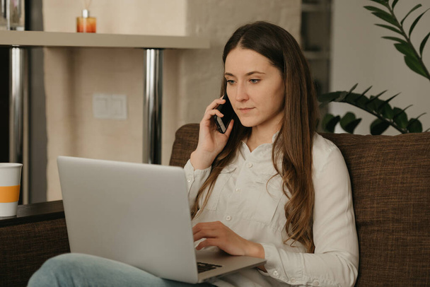 Praca zdalna. Biała kobieta studiująca zdalnie na laptopie. Kobieta z długimi włosami dzwoniąca z domu. - Zdjęcie, obraz
