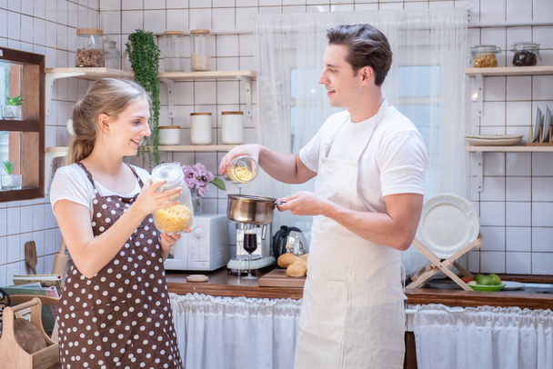 Onnellinen valkoihoinen pari perhe ruoanlaitto modernissa keittiössä kotona.Naimisissa romanttinen nainen halaa miestä leivän kanssa keittäessään tuoretta kasvissalaattia.
. - Valokuva, kuva