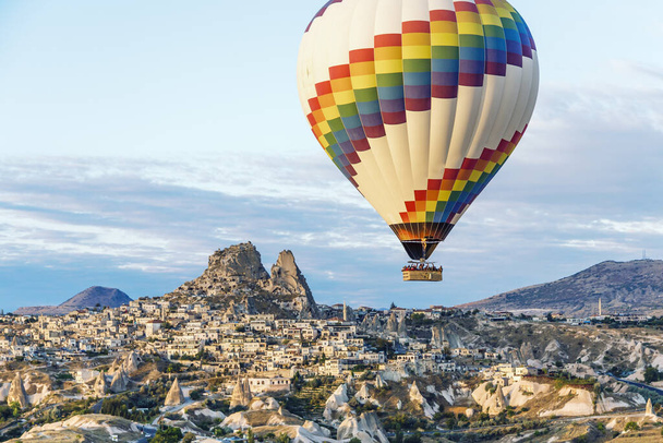 Πάνω από τα σπίτια των σπηλαίων και την πόλη της Καππαδοκίας στην Τουρκία επιπλέει ένα φωτεινό αερόστατο θερμού αέρα. - Φωτογραφία, εικόνα