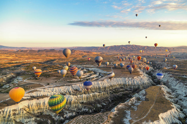 Φωτεινά και πολύχρωμα αερόστατα θερμού αέρα κατά την ανατολή που επιπλέουν κατά μήκος των κοιλάδων και των βουνών στην Καππαδοκία της Τουρκίας - Φωτογραφία, εικόνα