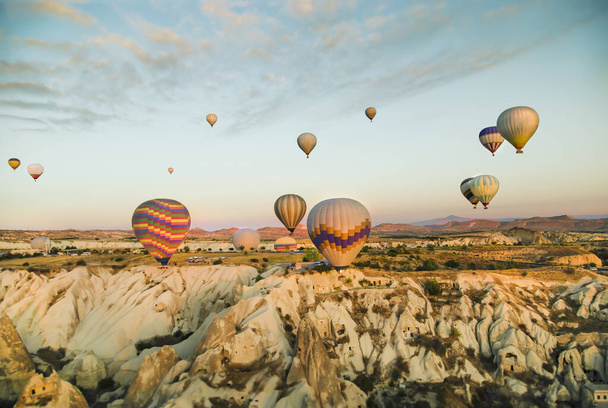 Φωτεινή ανατολή με πολύχρωμα αερόστατα θερμού αέρα την ανατολή να επιπλέουν κατά μήκος των σπηλαίων στην Καππαδοκία της Τουρκίας - Φωτογραφία, εικόνα