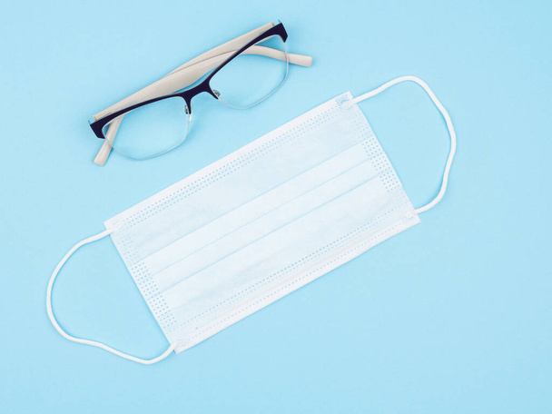 Brille und medizinische Maske auf blauem Hintergrund. - Foto, Bild