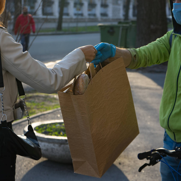 Delivery man give the online express order to receiver woman during the quarantine. Young beautiful woman receives her order from cheerful courier in medical mask and gloves.Food delivery concept. - Foto, imagen