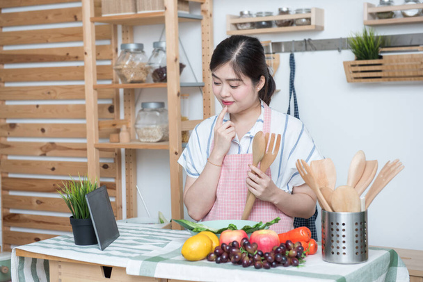 Mutlu Asyalı kadın evde yemek pişirmek için yemek arıyor, üniversite öğrencisi sosyal medya, sosyal mesafe, evde kalıp ev konseptinden uzakta çalışıyor.. - Fotoğraf, Görsel