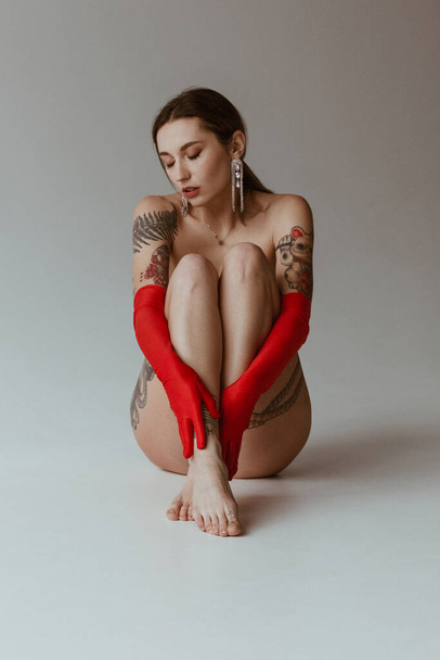 Sexy naked woman with tattoos wearing red gloves on white background - Photo, Image