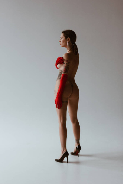 Sexy naked woman with tattoos wearing red gloves on white background - Foto, imagen
