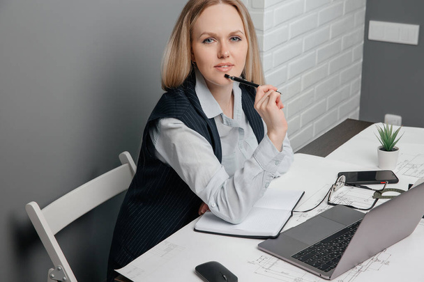 Beautiful business lady looks at camera and smiles sitting behind her workplace in office - Фото, зображення
