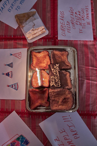 Torrija με κεριά για happy birhtday σε ένα κόκκινο τραπέζι και feltations χαρτιά - Φωτογραφία, εικόνα