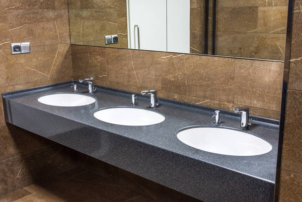 Pesutelineet, joissa on integroidut nestemäiset saippua-automaatit ja peili seinällä julkisessa wc-marmorissa
 - Valokuva, kuva