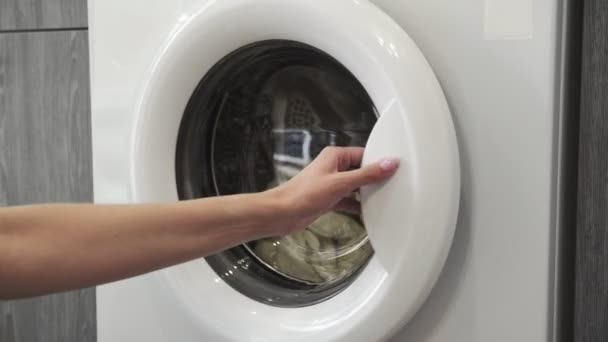 A női kéz kivesz két fehér SWEATert a mosógépből. Mosógép betöltése. Ruhákat a mosógépbe. Ruha mosógép betöltése. Mosás előkészítése - Felvétel, videó