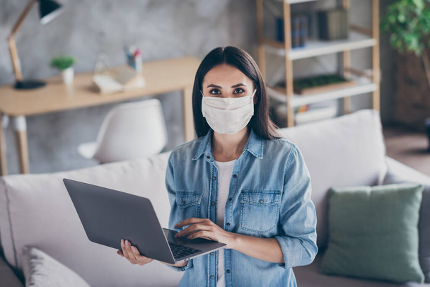 Portrait of positive girl self quarantine corona virus infection work home office use laptop wear medical mask jeans shirt in house indoors - 写真・画像