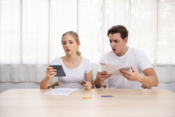 Young caucasian couple hand holding credit card and debt bill on table in home,men and women have overdue financial foreclosure problem sit in room with serious and unhappy payment. - Photo, Image