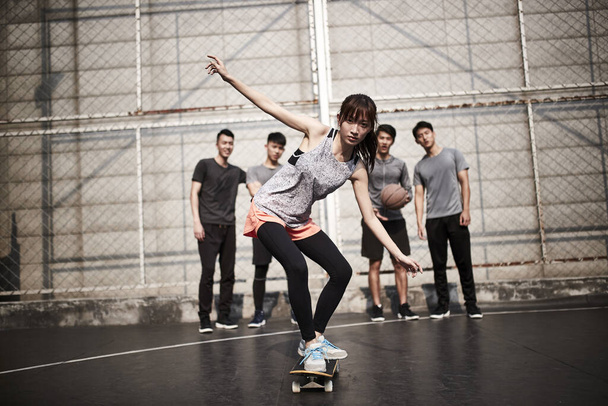 jong aziatische vrouw skateboarder skateboarden buiten met vrienden kijken van achteren - Foto, afbeelding