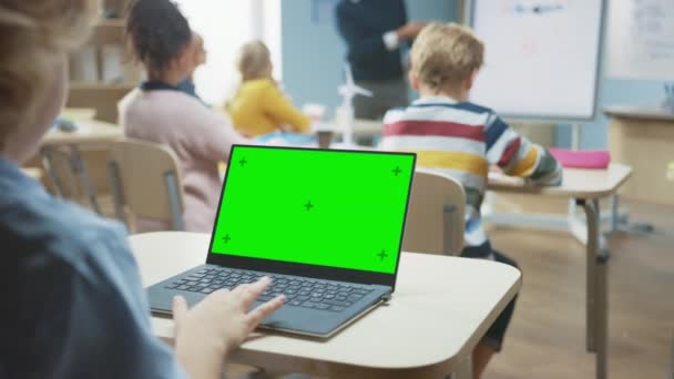Класс начальной школы: над плечом ребенка с помощью зеленого макета экрана ноутбука в классе. На заднем плане Учитель объясняет урок для разных классов
 - Кадры, видео